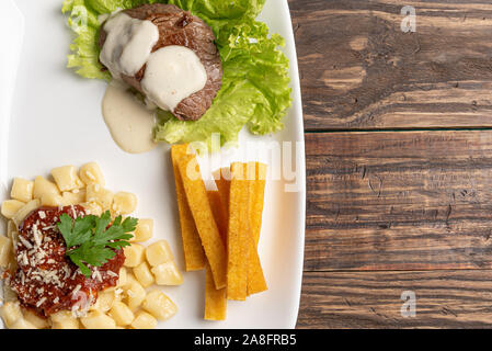 Des gnocchi faits maison avec de la sauce tomate et de la viande bovine mignon avec sauce au fromage dans une assiette blanche sur fond de bois Banque D'Images