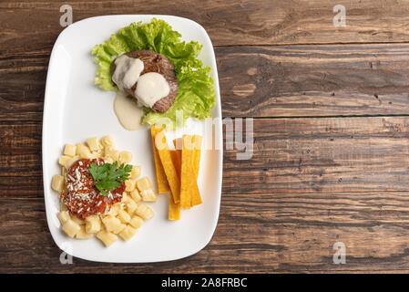 Des gnocchi faits maison avec de la sauce tomate et de la viande bovine mignon avec sauce au fromage dans une assiette blanche sur fond de bois Banque D'Images