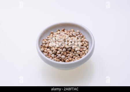 Matières premières non cuits Le sorgho (également connu sous le nom de sorgo) dans un bol blanc, isolé sur fond blanc Banque D'Images