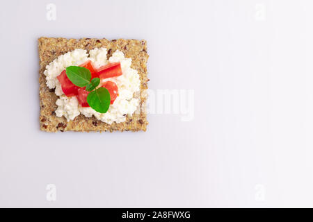 Le régime alimentaire des graines de lin craquelins à grains entiers avec du fromage ricotta, tomate et herbes isolé sur fond blanc, lumière douce Banque D'Images