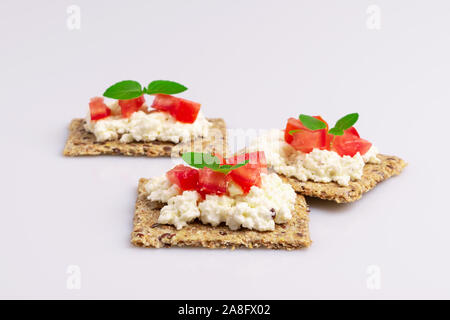 Le régime alimentaire des graines de lin craquelins à grains entiers avec du fromage ricotta, tomate et herbes isolé sur fond blanc, lumière douce Banque D'Images