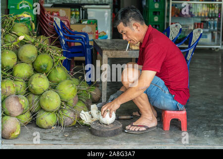 Nha Trang, Viêt Nam - Mars 11, 2019 : La cigarette réductions du vendeur de coco fraîchement récolté dans son magasin. Porte chemise rouge et bleu short. Banque D'Images