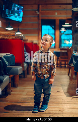 Cute adorable Portrait bébé garçon debout dans un café restaurant à la chaîne de télévision au programme. Kid trois ans intéressés en version électronique digita Banque D'Images