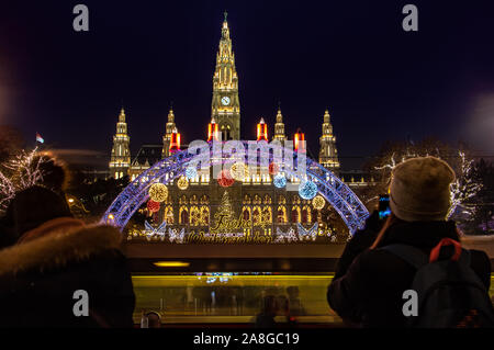 Les touristes prendre des photos l'illuminant la porte en face de la marché de Noël par City Hall - Nuit en hôtel de Vienne, Autriche. Banque D'Images