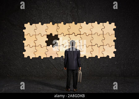 Un homme transportant une mallette ressemble à un puzzle accroché sur un mur avec une de ses pièces est manquant Banque D'Images