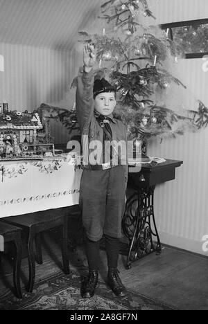 Un des membres de la jeunesse hitlérienne est avec un salut nazi devant l'arbre de Noël dans l'Allemagne des années 1930. Banque D'Images
