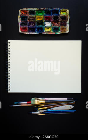 Artiste Créateur de travail télévision lay, immersive. Vue de dessus sur table avec carnet vierge, pinceaux et palettes de colorant. L'Art, atelier, peinture, dessin, Banque D'Images