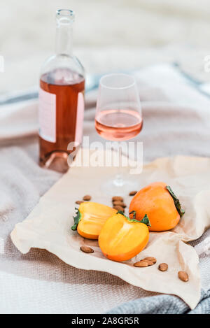 Pique-nique sur la plage avec les kakis, amande et bouteille de vin rose sur la couverture beige. Banque D'Images