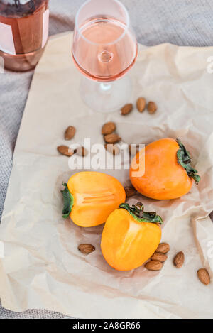 Pique-nique sur la plage avec les kakis, amande et bouteille de vin rose sur la couverture beige. Banque D'Images