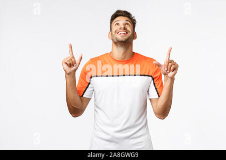 Surpris, heureux homme barbu à bonne en sports t-shirt, relever la tête et pointant vers le haut, étonné, souriant de bonheur et de joie, d'enthousiasme voir Banque D'Images