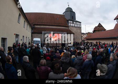 09 novembre 2019, la Thuringe, Großburschla : les visiteurs de l'Église s'asseoir et se tenir en face de l'église de Saint-Boniface pendant une émission en direct de l'ecumenical service divin. Les gouvernements d'état de Thuringe et de Hesse célébrons 30 ans de la chute du Mur de Berlin sous la devise '30 ans de la chute du mur - nous vivons la liberté'. Photo : Swen Pförtner/dpa Banque D'Images