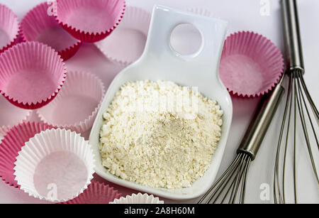 Tas de farine de blé dans un bol avec des tiges filetées pour battre les oeufs et le blanc du papier rose et moules pour muffins Banque D'Images