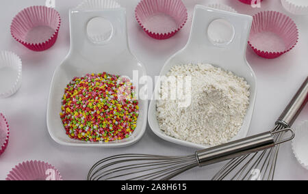 Tas de farine de blé et de sucre décoratif stars dans deux bols avec tiges pour battre les oeufs et le blanc du papier rose et moules pour muffins Banque D'Images