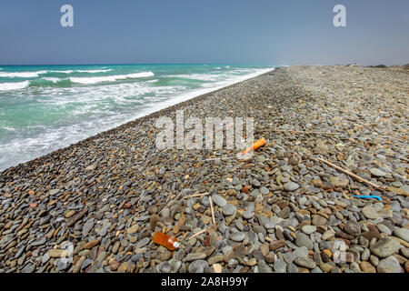 Divers déchets en plastique noir sauvage sauvage sur la plage de galets, pierre belle mer en arrière-plan. Banque D'Images