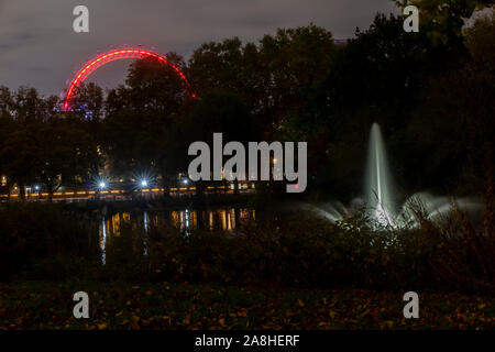 Une fontaine dans le lac à St James' Park la nuit avec le London Eye allumé au fond, derrière Horseguard's parade Banque D'Images