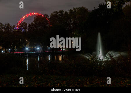 Une fontaine dans le lac à St James' Park la nuit avec le London Eye allumé au fond, derrière Horseguard's parade Banque D'Images