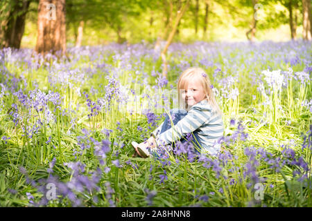 Une mignonne petite fille assise parmi les jacinthes dans les bois, forêt, Essex Banque D'Images