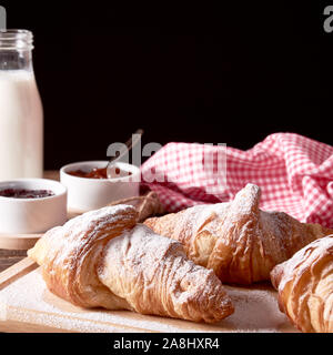 Still Life with french croissants sucrés, verre de lait et un bol de confiture sur la vieille planche de bois et fond noir. L'espace pour votre texte. Banque D'Images