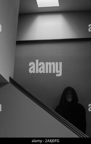 Moine à capuchon, debout dans la lumière de l'apparition de la fenêtre au pied de l'escalier Banque D'Images