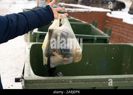 La main d'un homme dans le trigger en hiver met le sac dans la poubelle.Closeup hand holding morceau d'ordures dans la poubelle. Banque D'Images