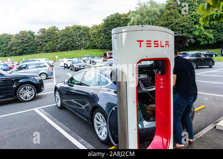 Les frais d'un homme sa voiture à la station de charge de Tesla à l'autoroute au Royaume-Uni, de charge électrique Banque D'Images