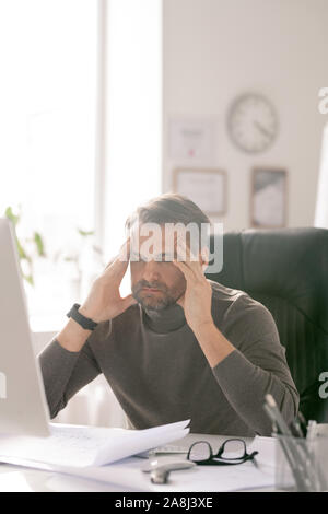 Homme mature fatigué avec ses yeux fermés essayant de se concentrer par lieu de travail Banque D'Images