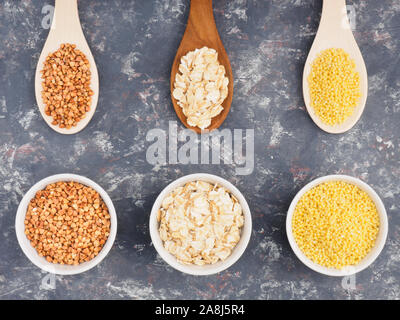 Les gruaux d'avoine, millet, sarrasin blanc dans des tasses et des cuillères en bois sombre sur un fond en béton. Notion de perte de poids Banque D'Images