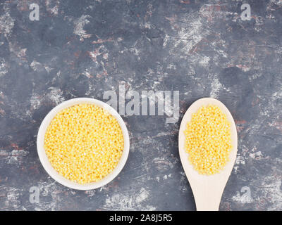 Millet en blanc tasses de gruau et de cuillères en bois sur un fond de béton foncé. Notion de perte de poids Banque D'Images