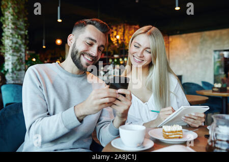 Young cheerful couple looking at smartphone écran tout en restant assis dans le café Banque D'Images