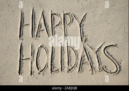 Message joyeuses Fêtes en grandes lettres manuscrites en capital sur une plage de sable fin Banque D'Images