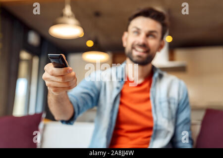 Lieu de loisirs à la maison. Jeune homme assis sur le canapé à regarder la télévision avec télécommande Câble de commutation close-up arrière-plan flou smiling happy Banque D'Images