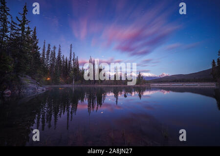 Avant le lever du soleil à Pyramid Lake. Comme les eaux miroir reflète, montagnes, arbres et nuages. Heure bleue et calme matin. Le Parc National de Jasper, Canada. Banque D'Images