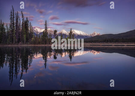 Avant le lever du soleil à Pyramid Lake. Comme les eaux miroir reflète, montagnes, arbres et nuages. Heure bleue et calme matin. Le Parc National de Jasper, Canada. Banque D'Images