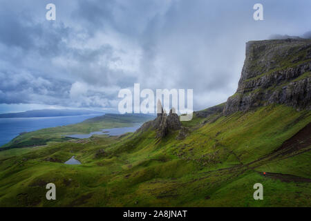 Old Man Storr. Le Storr sous un ciel nuageux dans un jour de pluie. Personne avec veste orange de la randonnée à travers l'herbe sous la pluie. Île de Skie, en Écosse. Banque D'Images