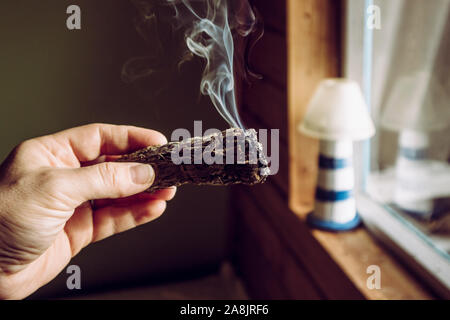 Woman hand holding herb paquet de sauge séchée smudge stick de fumer. On pense à nettoyer l'énergie négative et purifier les espaces de vie à la maison dans les chambres Banque D'Images