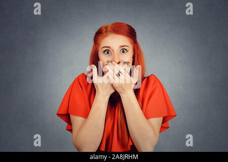 Femme occupe ses mains sur la bouche, le couvrant, les yeux grands ouverts dans l'anéantissement fond rouge isolé. Redhead girl couvrant la bouche avec les mains et regardant Banque D'Images