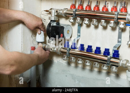 Un travailleur est l'installation d'une tête thermique sur le distributeur du système de chauffage. Banque D'Images