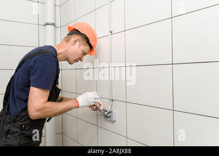 L'électricien est d'installer une prise électrique murale. Banque D'Images