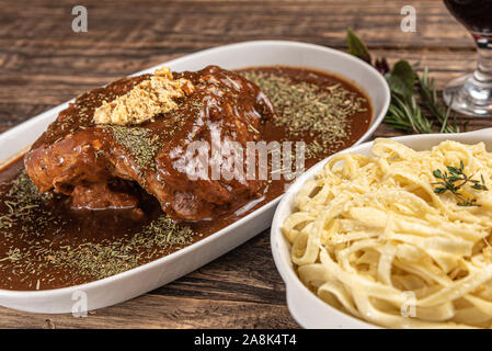 Des pâtes avec du bœuf mignon sauce sombre dans une assiette blanche sur fond blanc en bois, lumière douce, Banque D'Images