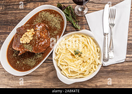 Des pâtes avec du bœuf mignon sauce sombre dans une assiette blanche sur fond blanc en bois, lumière douce, Banque D'Images