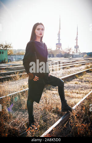 Fashion shot : portrait de la jolie fille rock (modèle informel) dans une tunique et un pantalon en cuir debout à rails (zone industrielle) Banque D'Images