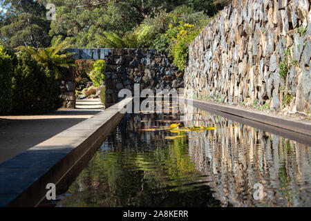 L'étang de l'eau jardin avec mur de roche, nénuphars, arche porte le long de la passerelle en pierre entourée d'arbres Banque D'Images