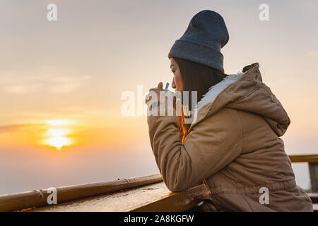 Une femme asiatique se trouve le café au lever du soleil sur le sommet d'une montagne. Banque D'Images