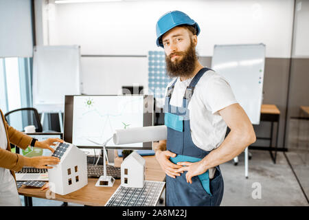 Portrait d'un travailleur barbu en vêtements et casque de protection debout dans l'énergie alternative design office Banque D'Images