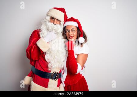 L'âge moyen couple wearing Santa costume hugging sur fond blanc isolé with hand on chin la réflexion sur la question, l'expression pensive. Smiling Banque D'Images