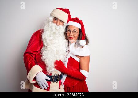 L'âge moyen couple wearing Santa costume hugging sur fond blanc isolé à sourire sur le côté et a fixer loin de penser. Banque D'Images