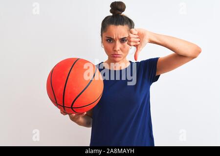 Jeunes et belles de la sportive holding basketball ball sur fond blanc isolé, visage en colère avec signe négatif montrant non avec Thumbs down, re Banque D'Images