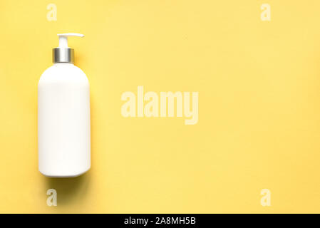 Distributeur blanc sur fond jaune, vue du dessus, copiez l'espace. Flacon pompe en plastique blanc et crème de shampoing ou du savon, soin de concept. Banque D'Images