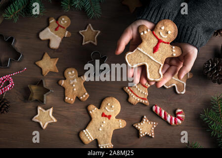 Hands holding Christmas gingerbread cookie, décoré gingerman sur fond de bois, vue du dessus, copiez l'espace. D'épices de Noël dans les mains de l'enfant. Banque D'Images