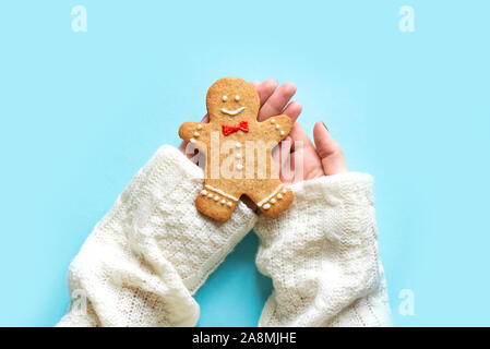 Gingerbread Man dans les mains sur fond bleu. Noël à la mode composition minimale - mains tenant des gingerbread man cookie, vue d'en haut. Banque D'Images